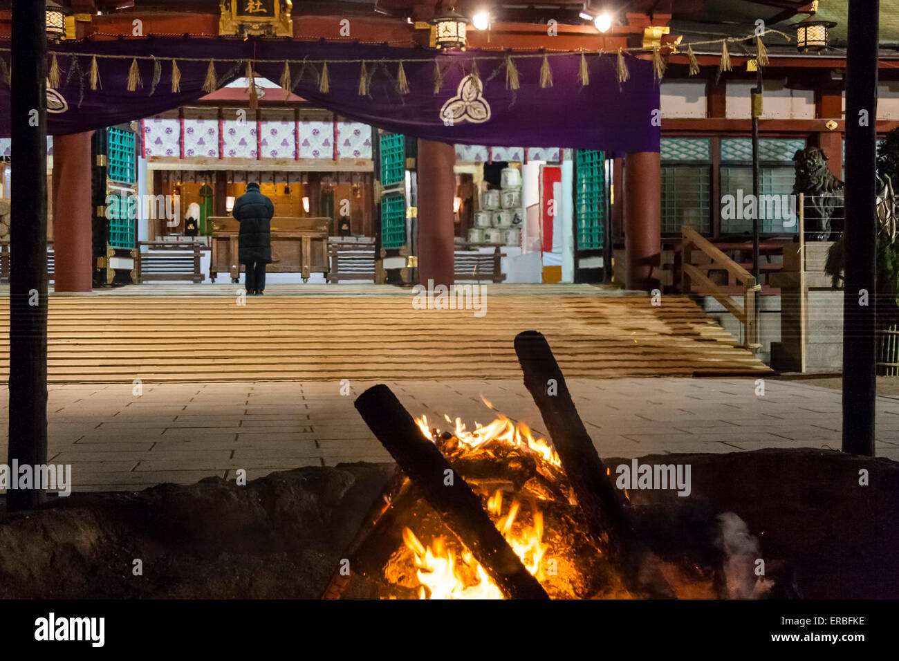 Capodanno al santuario di Shinto Nishinomiya in Giappone. Prima serata davanti alla folla. Falò in primo piano con l'uomo solista che si oppone alla sala del santuario. Foto Stock