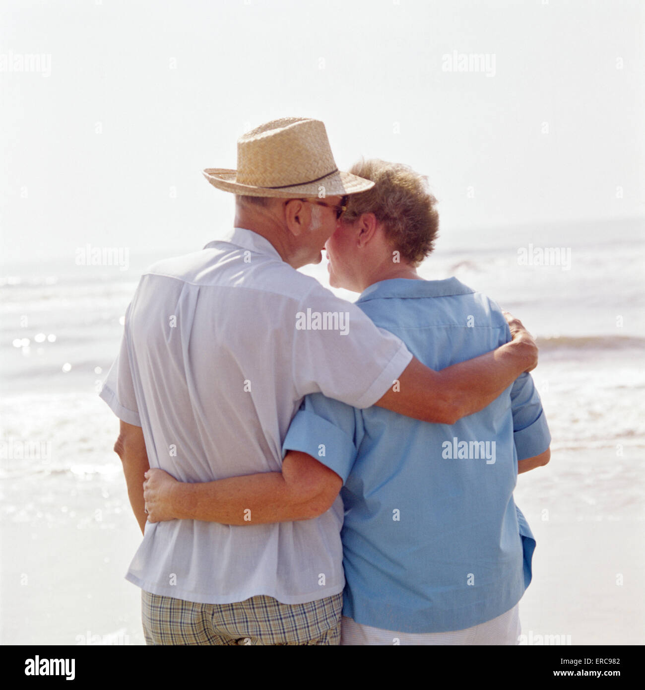 Anni Settanta VISTA POSTERIORE COPPIA IN PENSIONE SULLA SPIAGGIA UOMO WHISPERING PER DONNA Foto Stock