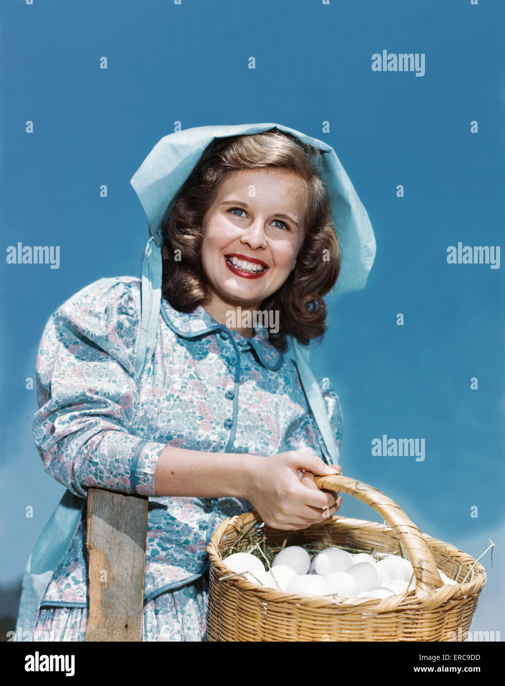 Negli anni quaranta anni cinquanta sorridente ragazza adolescente che indossa la ragazza di fattoria PIONEER OUTFIT ABITO CALICO COFANO cestello di contenimento di uova Foto Stock