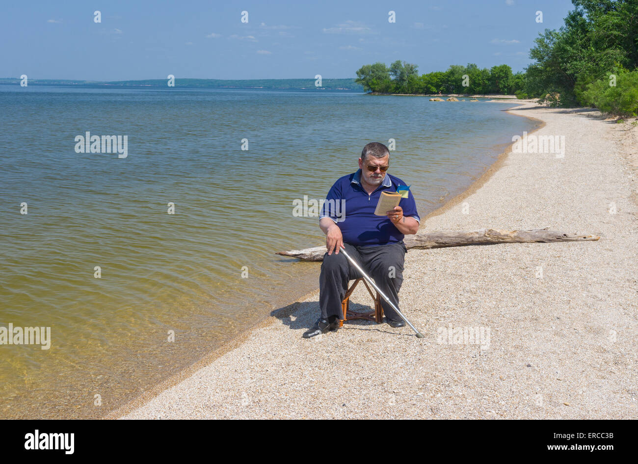 Senior uomo lettura libro seduti su una spiaggia del fiume Dnepr in Ucraina Foto Stock