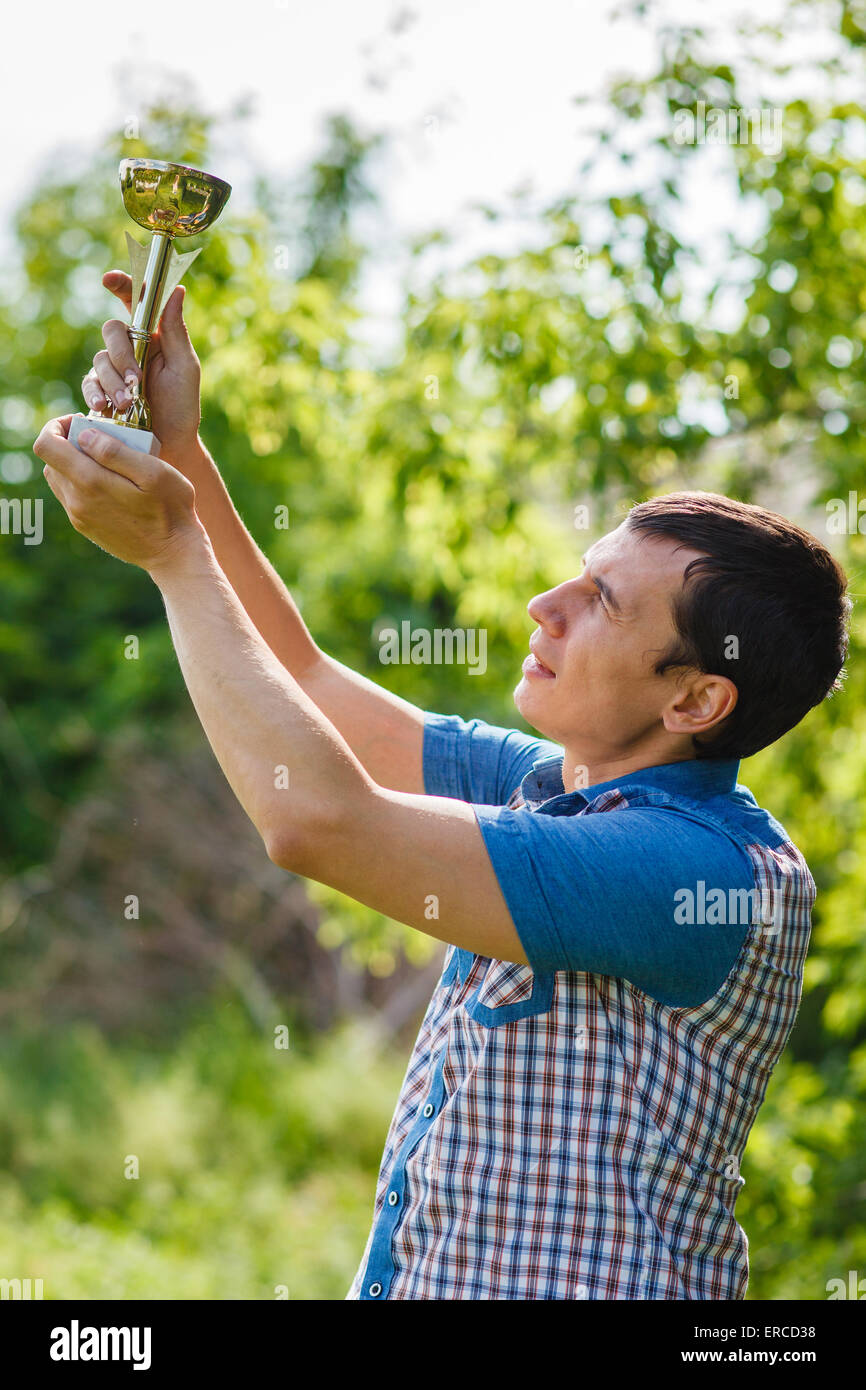 L'uomo tenendo un sports cup su strada la vittoria contro il verde Foto Stock