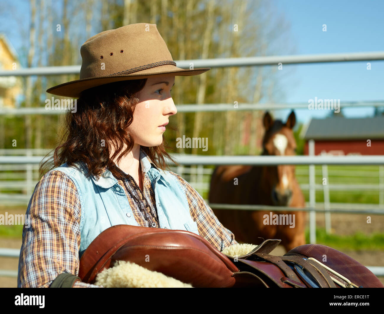 Cowgirl portante una sella di cavallo in un paddock Foto Stock