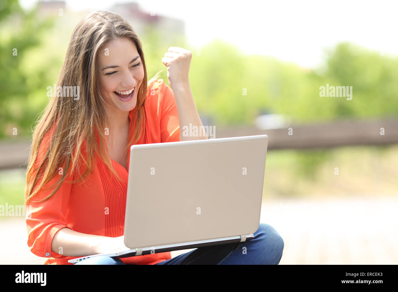 Euforico donna ricerca lavoro con un computer portatile in un parco urbano in estate Foto Stock