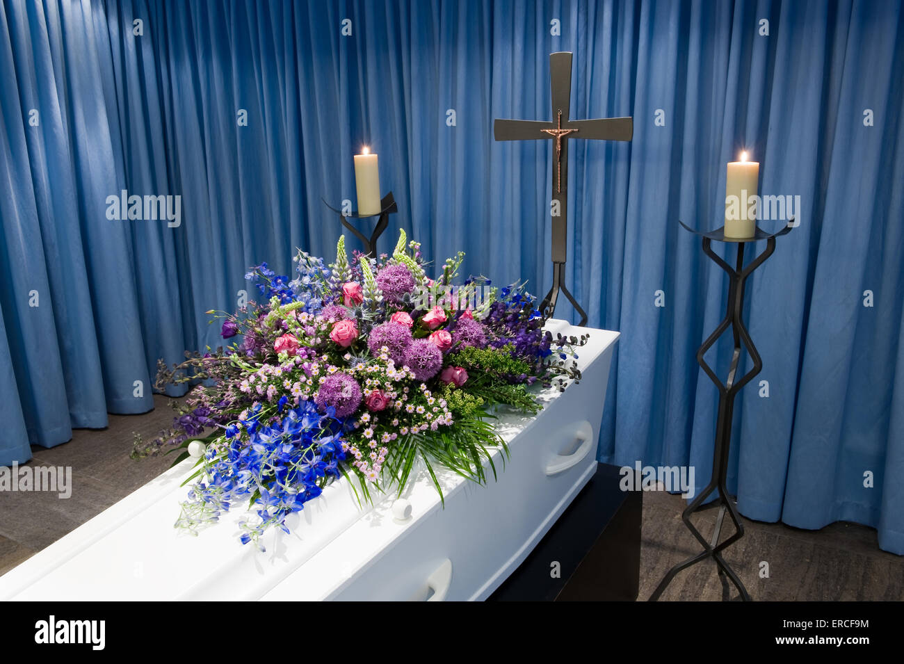 Una bara con un omaggio floreale in un obitorio con due candele accese e una croce Foto Stock