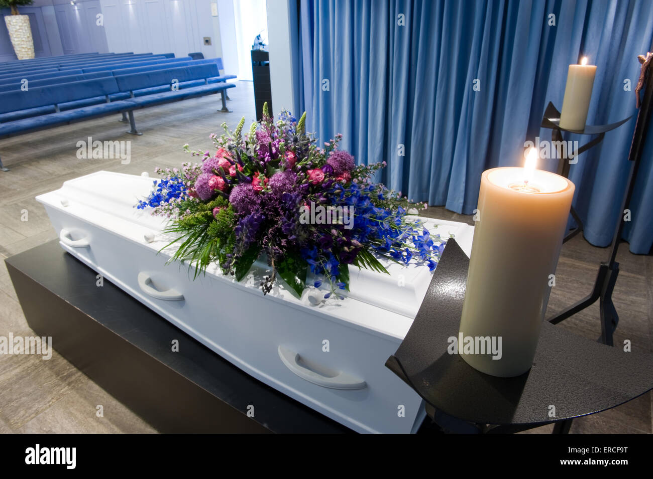 Una bara con un omaggio floreale in un obitorio con due candele accese Foto Stock