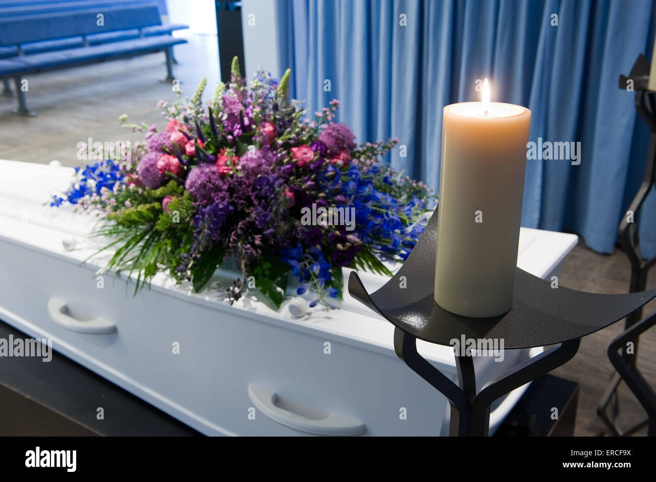 Una bara con un omaggio floreale in un obitorio e una candela che brucia Foto Stock