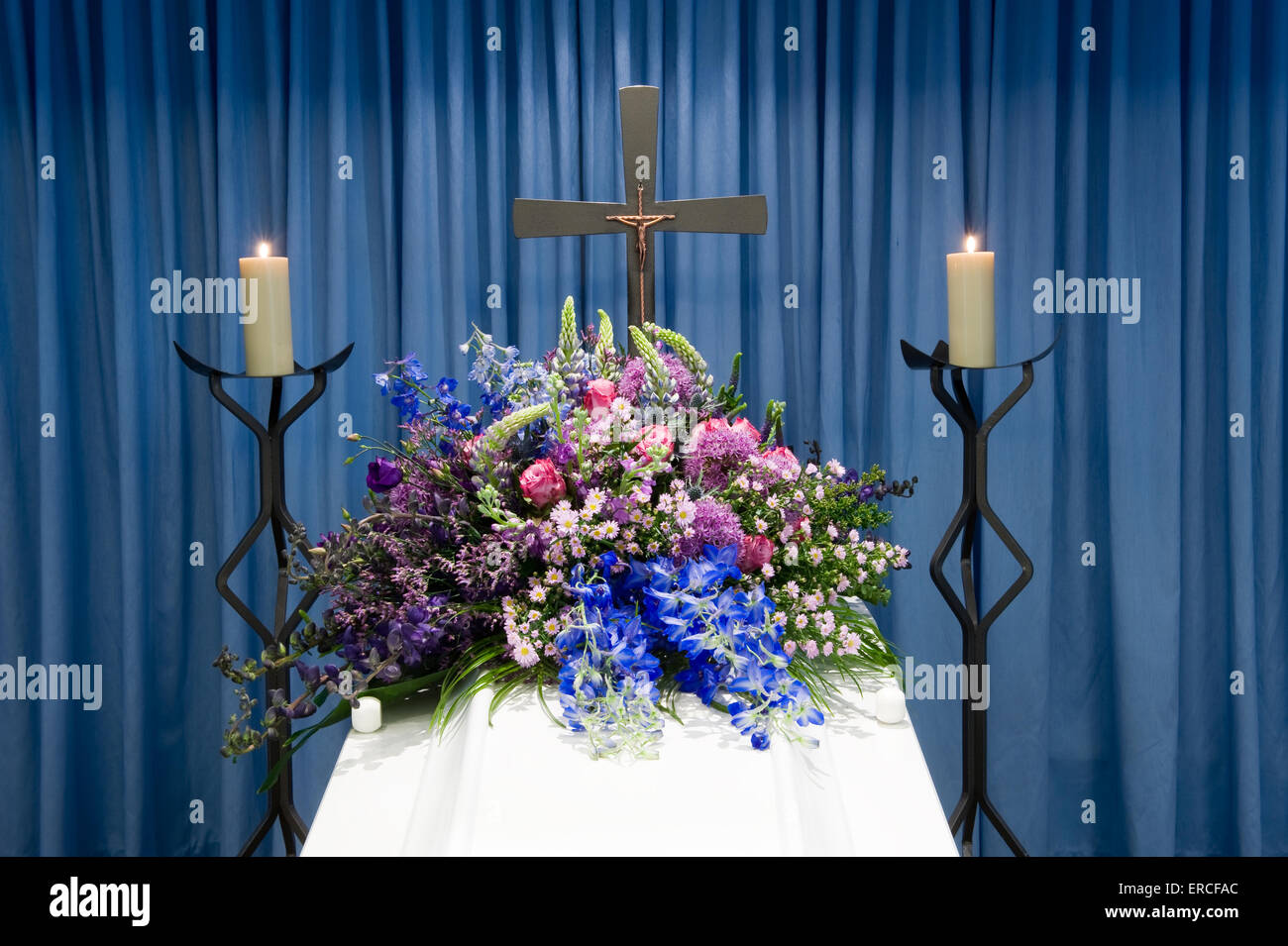 Una bara con un omaggio floreale in un obitorio con due candele accese e una croce Foto Stock