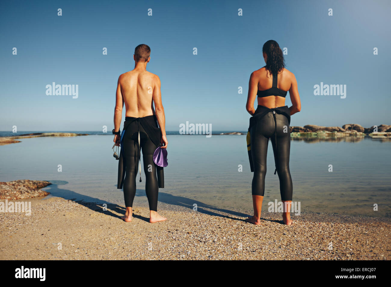 Vista posteriore dei giovani atleti in piedi sul lago di preparazione per il triathlon. L uomo e la donna della preparazione di una gara che indossa una muta. Foto Stock