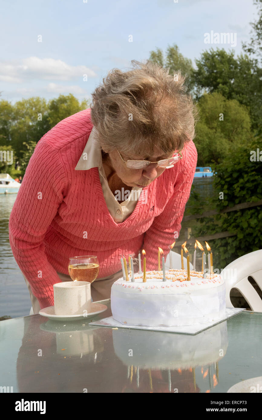 Una matura pensionati anziani donna soffiando le candeline sulla sua torta di compleanno, REGNO UNITO Foto Stock