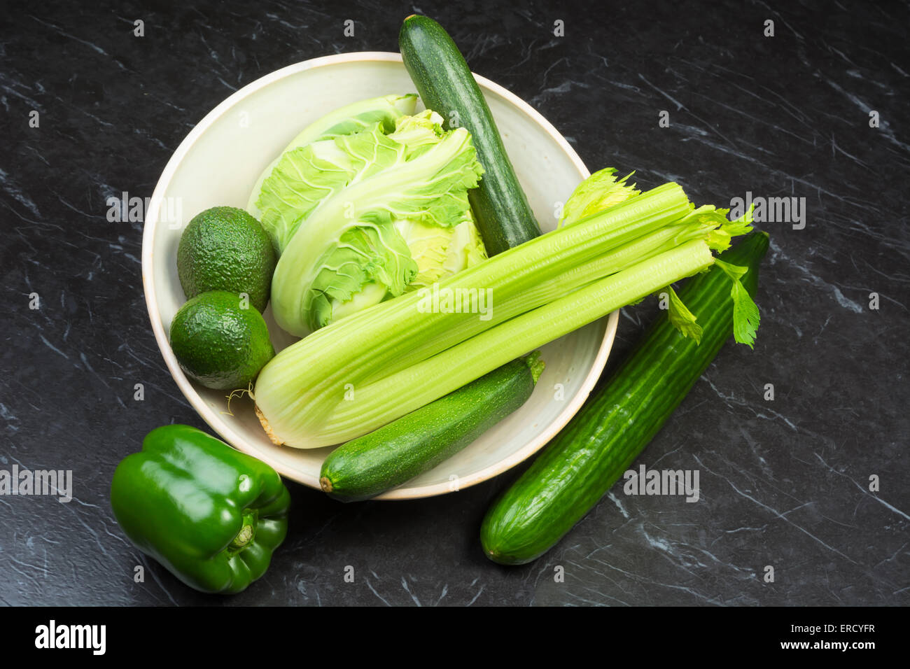 Un assortimento di verdure fresche a foglia verde in un vaso di ceramica su una pietra nera superficie Foto Stock