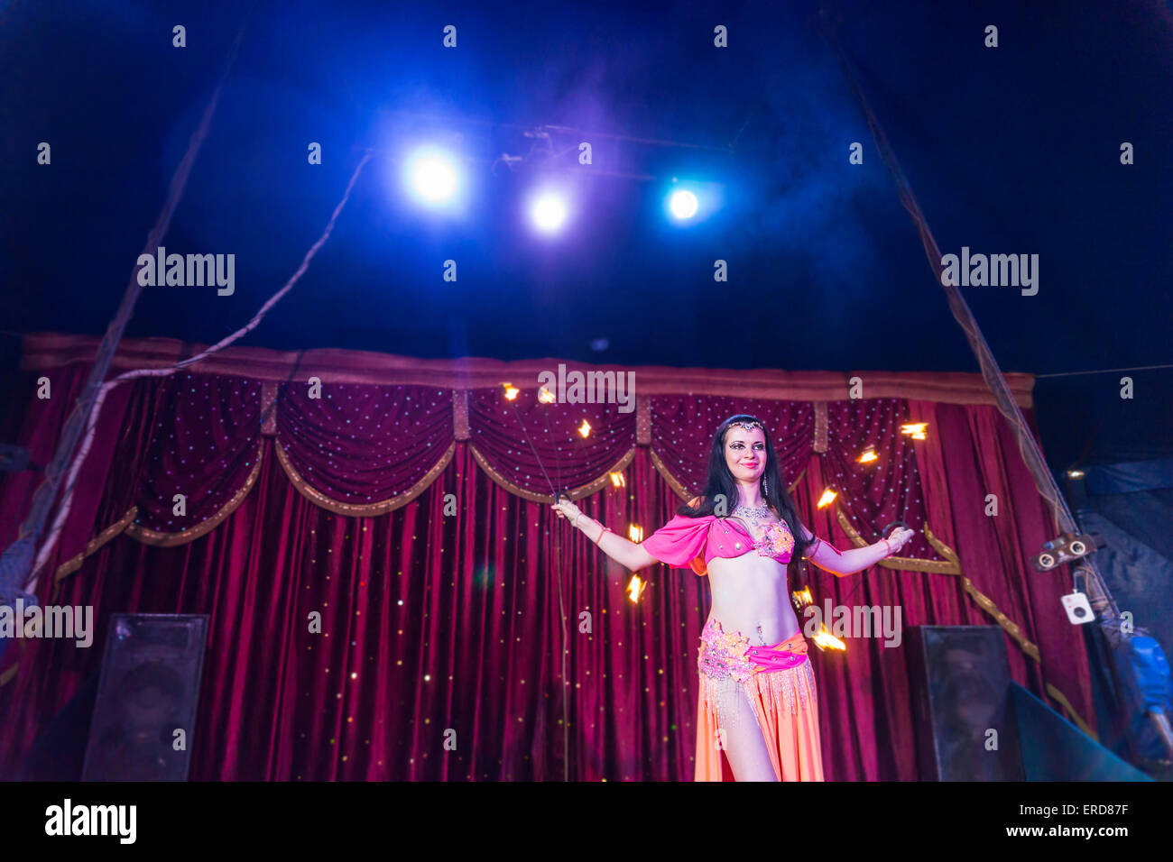 Basso angolo di vista esotici dai capelli scuri femmina ballerino incendio indossando rosa luminoso e Costume arancione fa roteare due Flaming Baton Appara Foto Stock