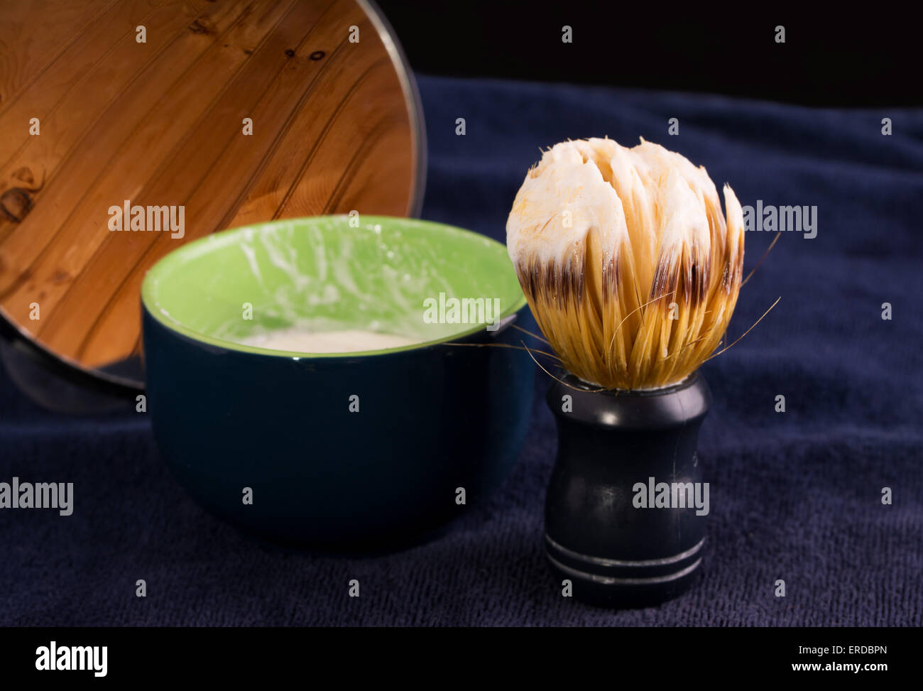 Spazzola per la rasatura con schiuma di sapone, bicchiere e specchio sul blu scuro asciugamano Foto Stock