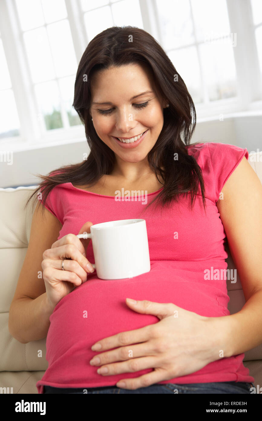 Donna incinta di bere una bevanda calda a casa Foto Stock