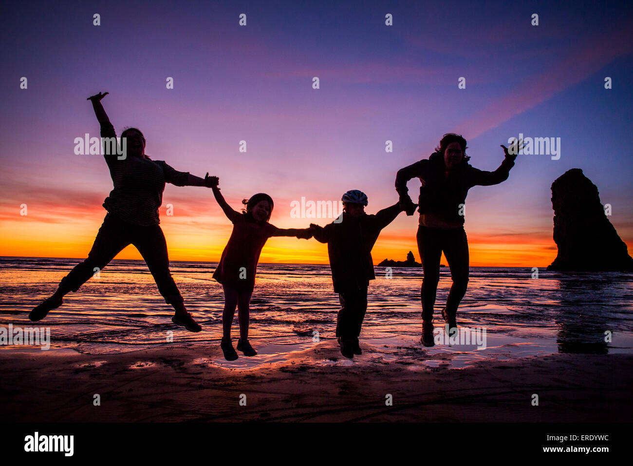 Silhouette della famiglia caucasica salti di gioia sul Cannon Beach, Oregon, Stati Uniti Foto Stock