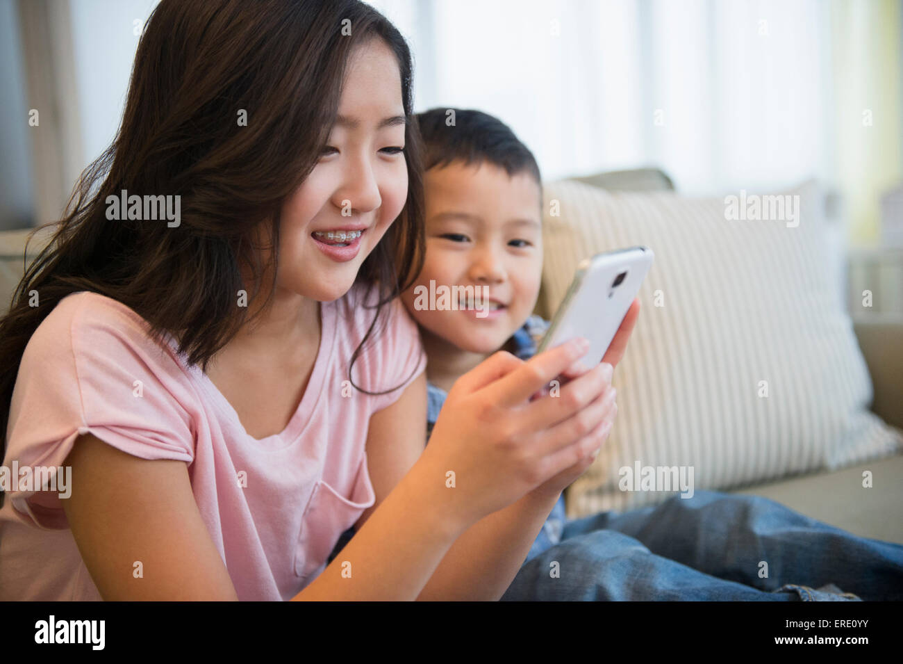 Asian fratello e sorella tramite telefono cellulare sul divano Foto Stock