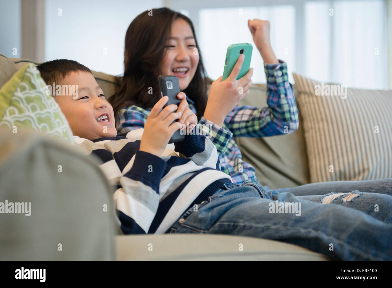Asian fratello e sorella utilizzando i telefoni cellulari sul divano Foto Stock
