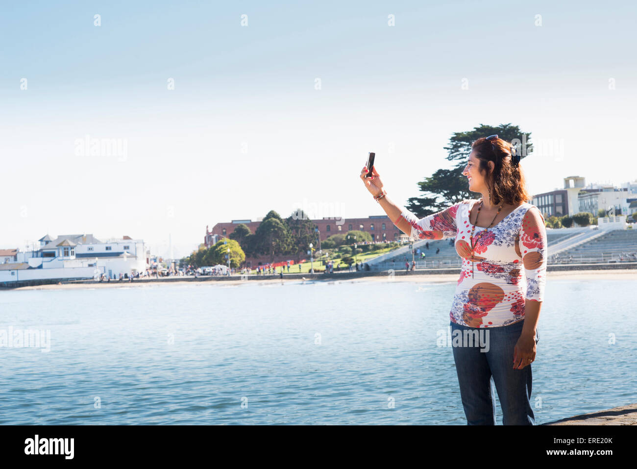 Donna ispanica tenendo cellulare selfie a waterfront Foto Stock