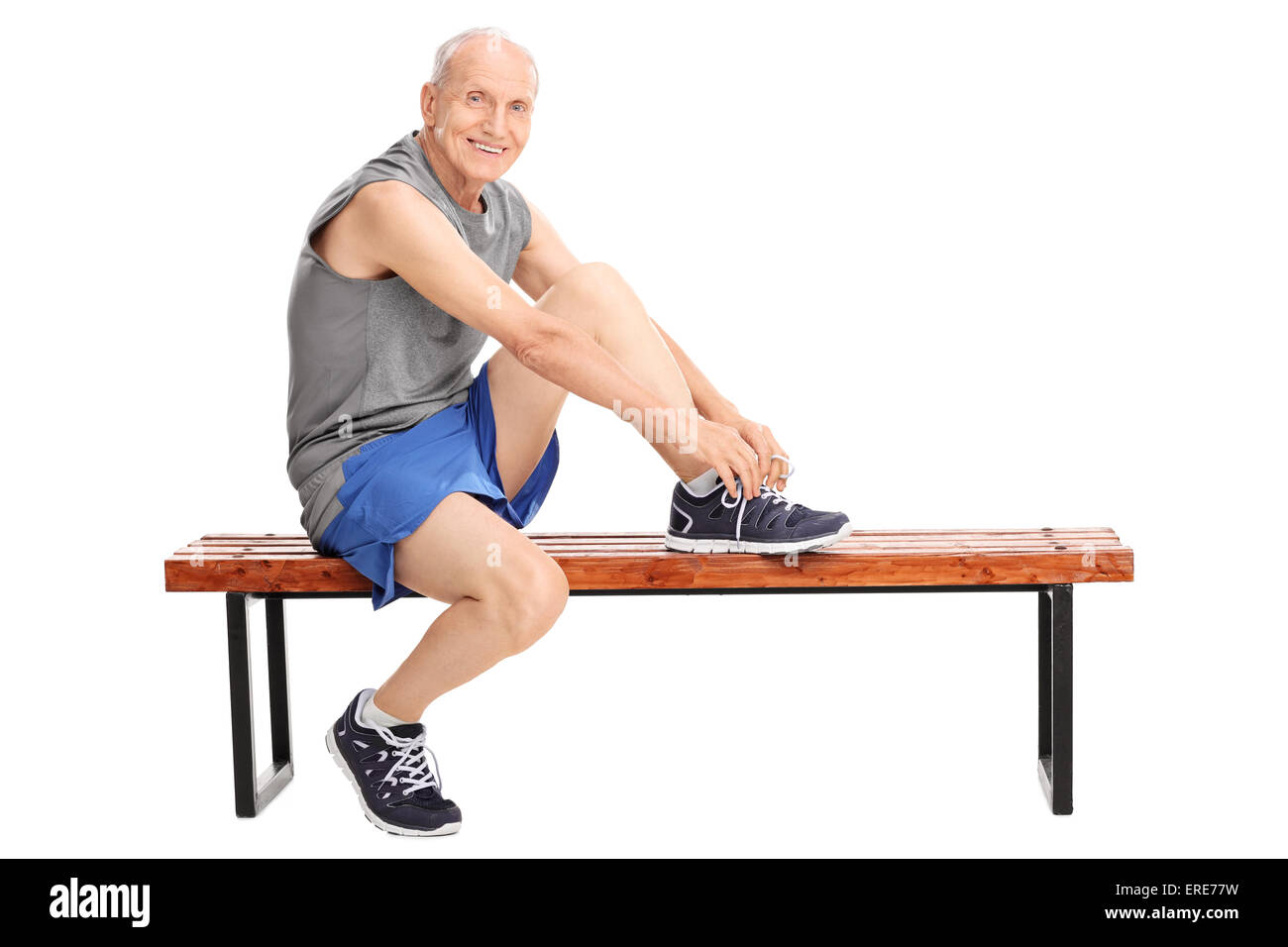 Studio shot di un allegro senior in legatura di abbigliamento sportivo i suoi lacci delle scarpe seduto su una panchina e guardando la telecamera Foto Stock