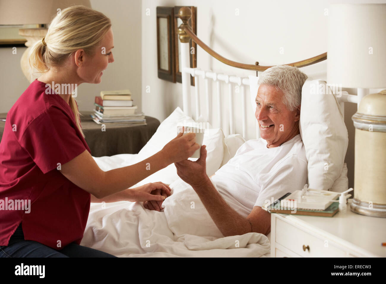 Salute visitatore dando maschio Senior bevanda calda nel letto di casa Foto Stock