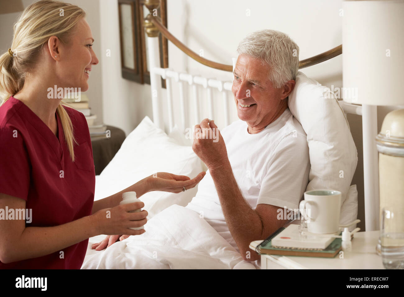 Salute visitatore dando Senior farmaco maschio nel letto di casa Foto Stock