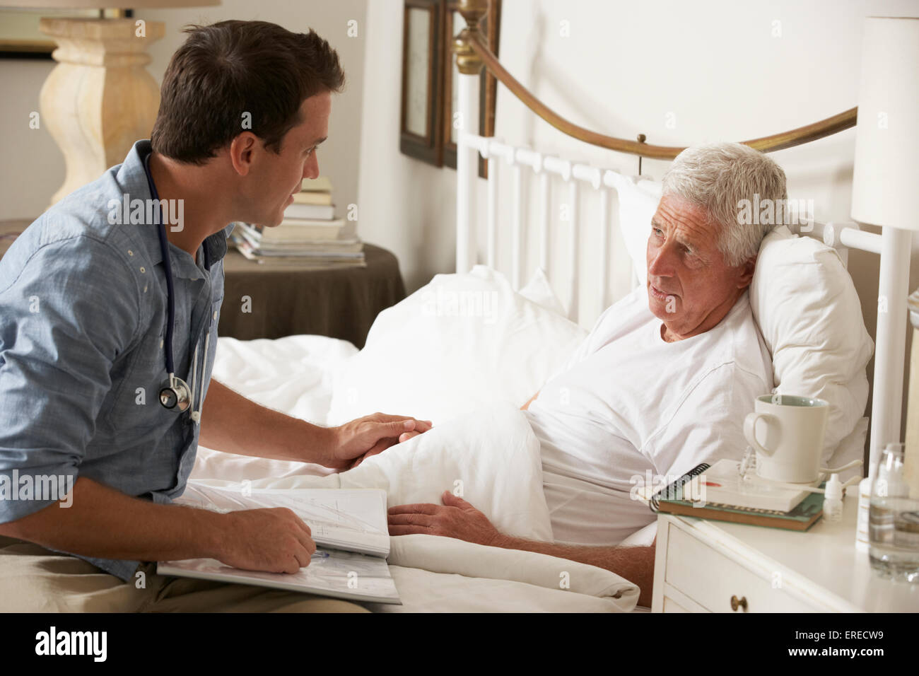 Medico di parlare con i Senior paziente di sesso maschile nel letto di casa Foto Stock
