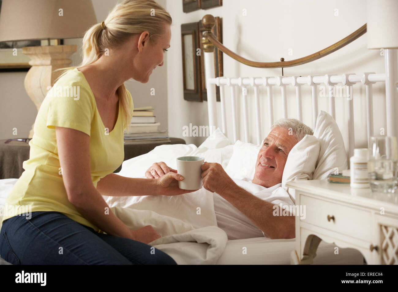 Figlia adulta dando Senior genitore maschile bevanda calda nel letto di casa Foto Stock