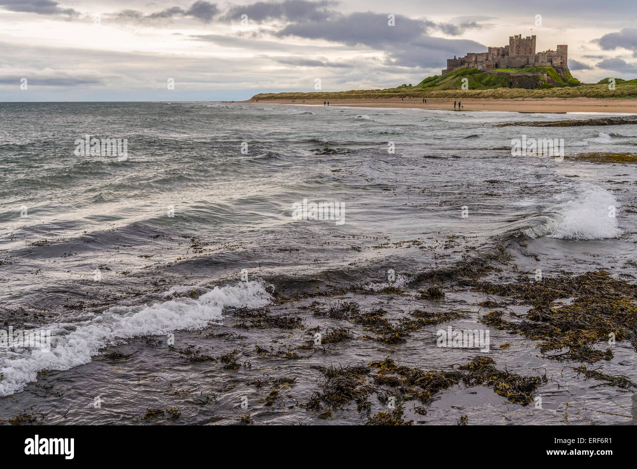 Il castello di Bamburgh Northumberland. Inghilterra del nord est. onde sulla spiaggia invernale giorno grigio Foto Stock
