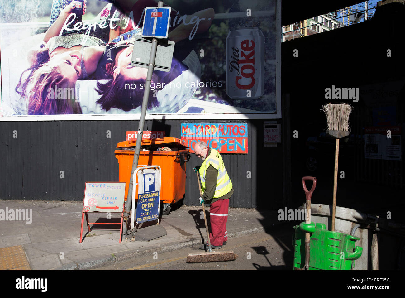 Pulitore di via spazzare vicino ad un cartellone pubblicitario su un angolo di strada sul cavo Street, Londra, Regno Unito. Foto Stock