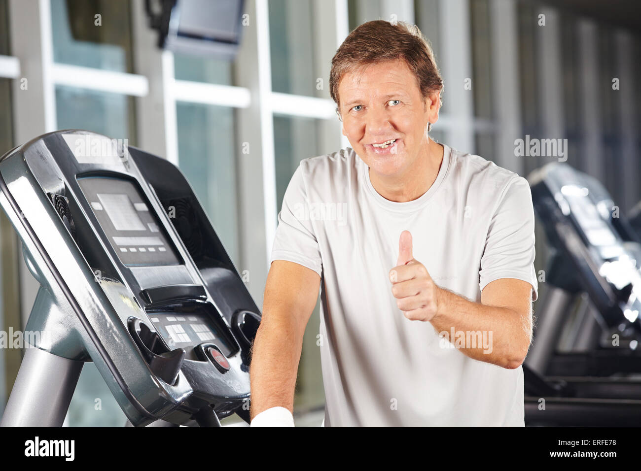 Uomo anziano tenendo le dita fino in centro fitness su un tapis roulant Foto Stock