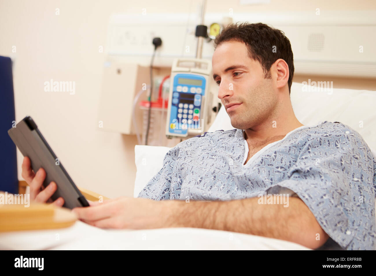 Paziente di sesso maschile con tavoletta digitale nel letto di ospedale Foto Stock