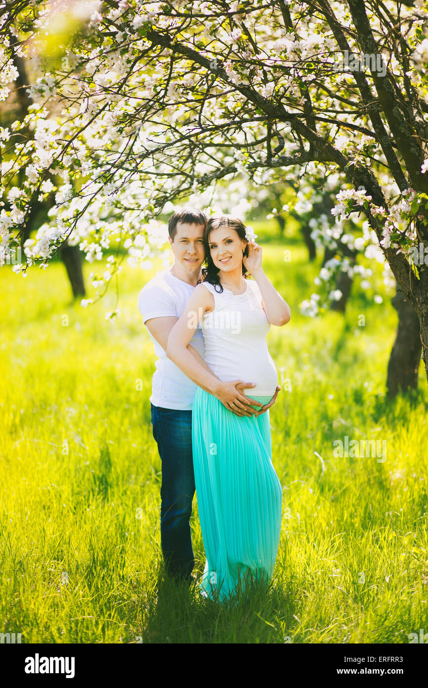 Ritratto di felice famiglia in gravidanza. Donna incinta e uomo in piedi in primavera in fiore giardino nella giornata di sole. Due persone nell'amore. Foto Stock