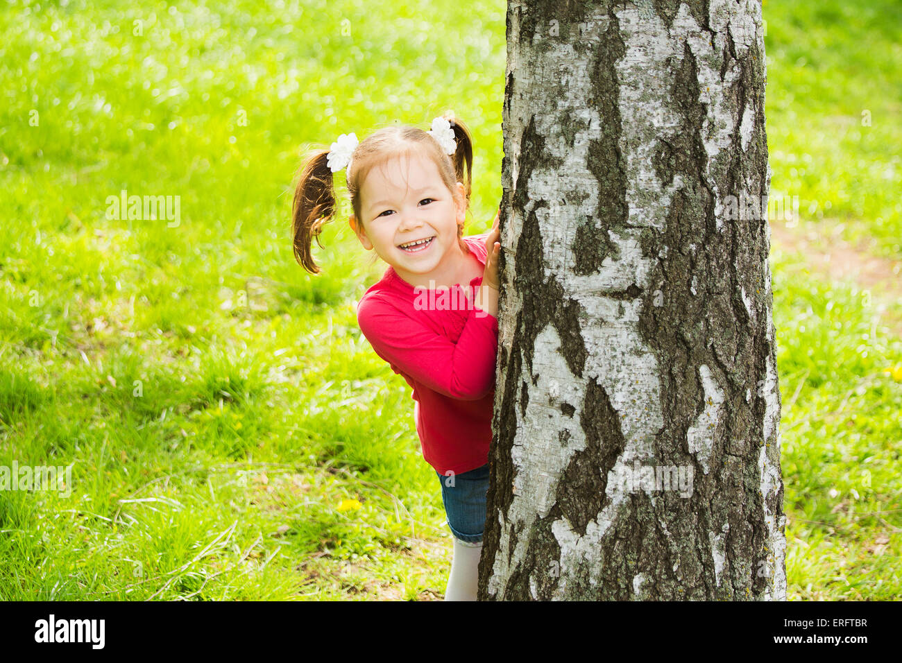 Carino bambina nascosto dietro un enorme albero. Bambini Ritratto guardando la fotocamera Foto Stock