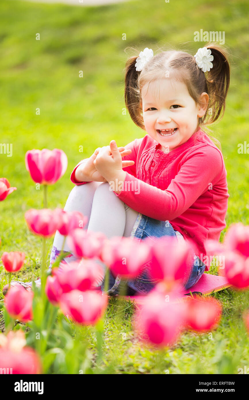 Allegro poco ragazza seduta in erba guardando i tulipani . bambino gioca al di fuori Foto Stock