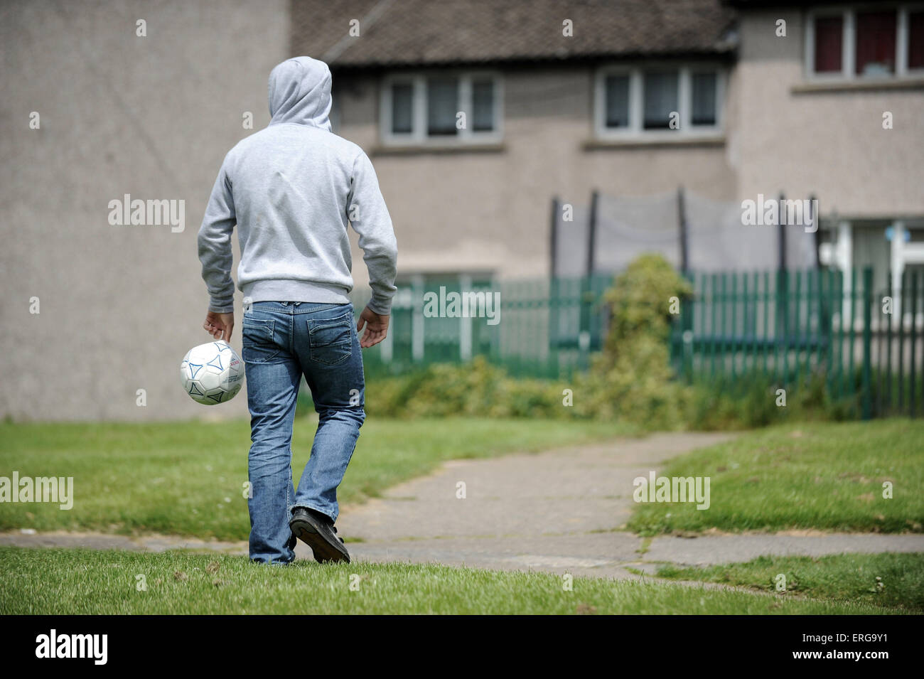 Una gioventù maschile porta un calcio su una corsa verso il basso complesso residenziale sulla Gurnos estate in Merthyr, nel Galles del Sud. Foto Stock