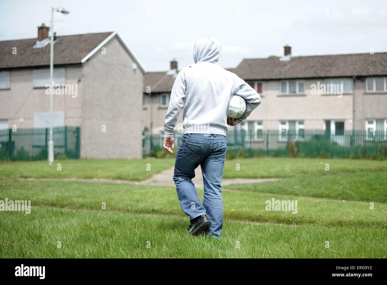 Una gioventù maschile porta un calcio su una corsa verso il basso complesso residenziale sulla Gurnos estate in Merthyr, nel Galles del Sud. Foto Stock