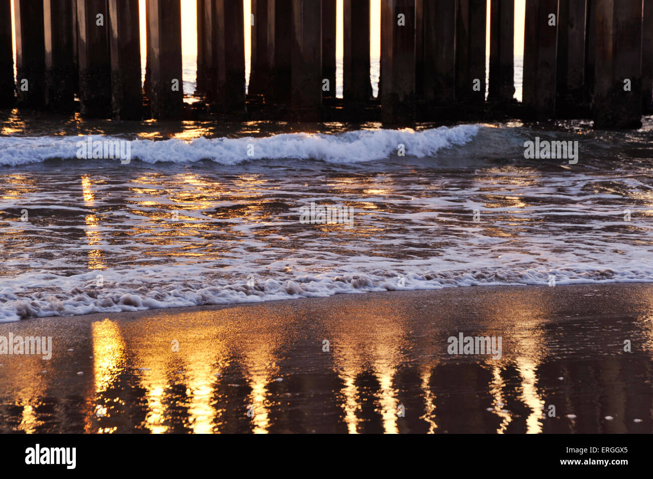 Golden riflesso del sole e colonne di cemento del molo sul bagnato di sabbia sulla spiaggia dove le onde sono il lavaggio contro la riva Foto Stock