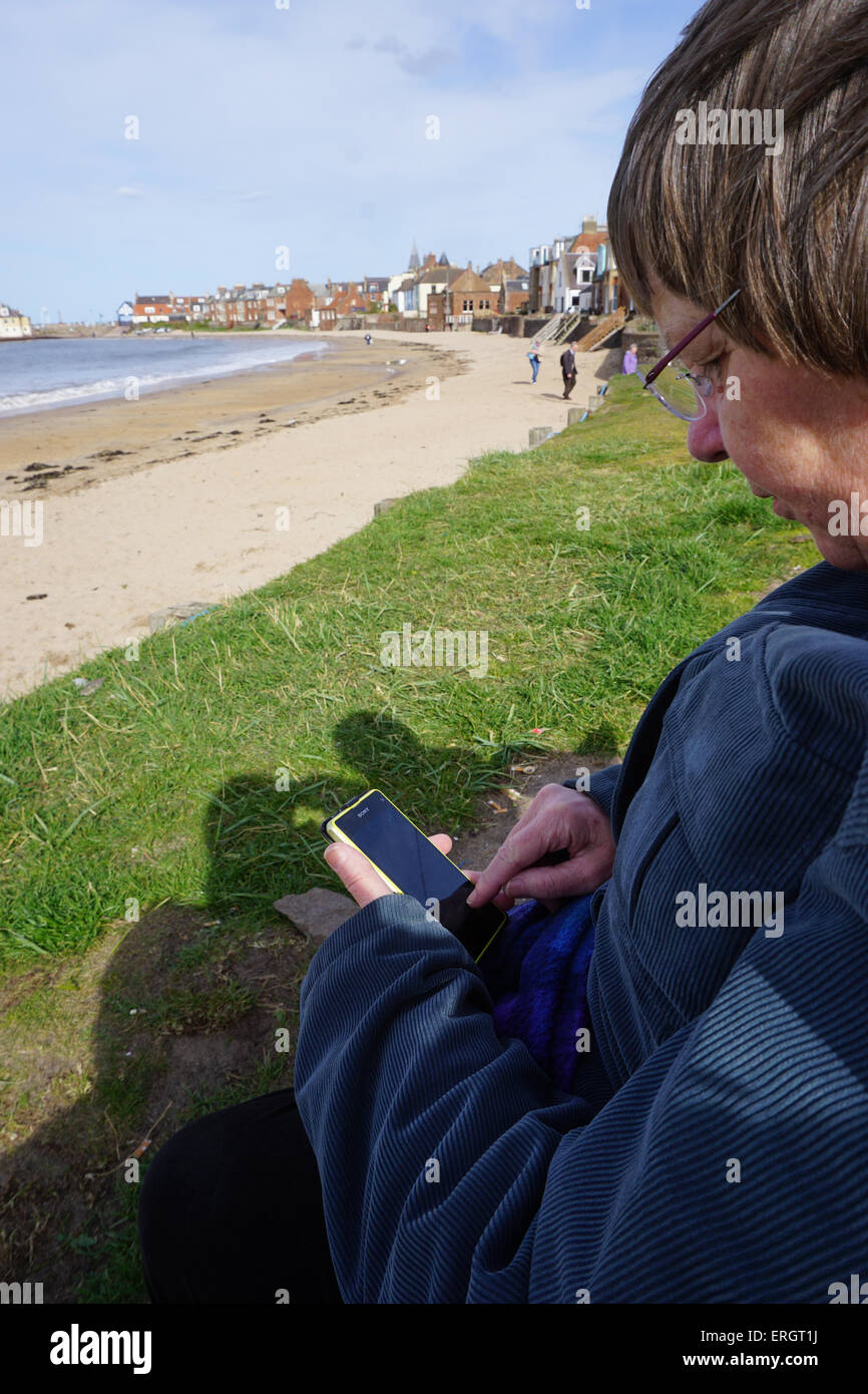 La donna seduta vicino alla spiaggia utilizza lo smartphone per accedere a internet Foto Stock