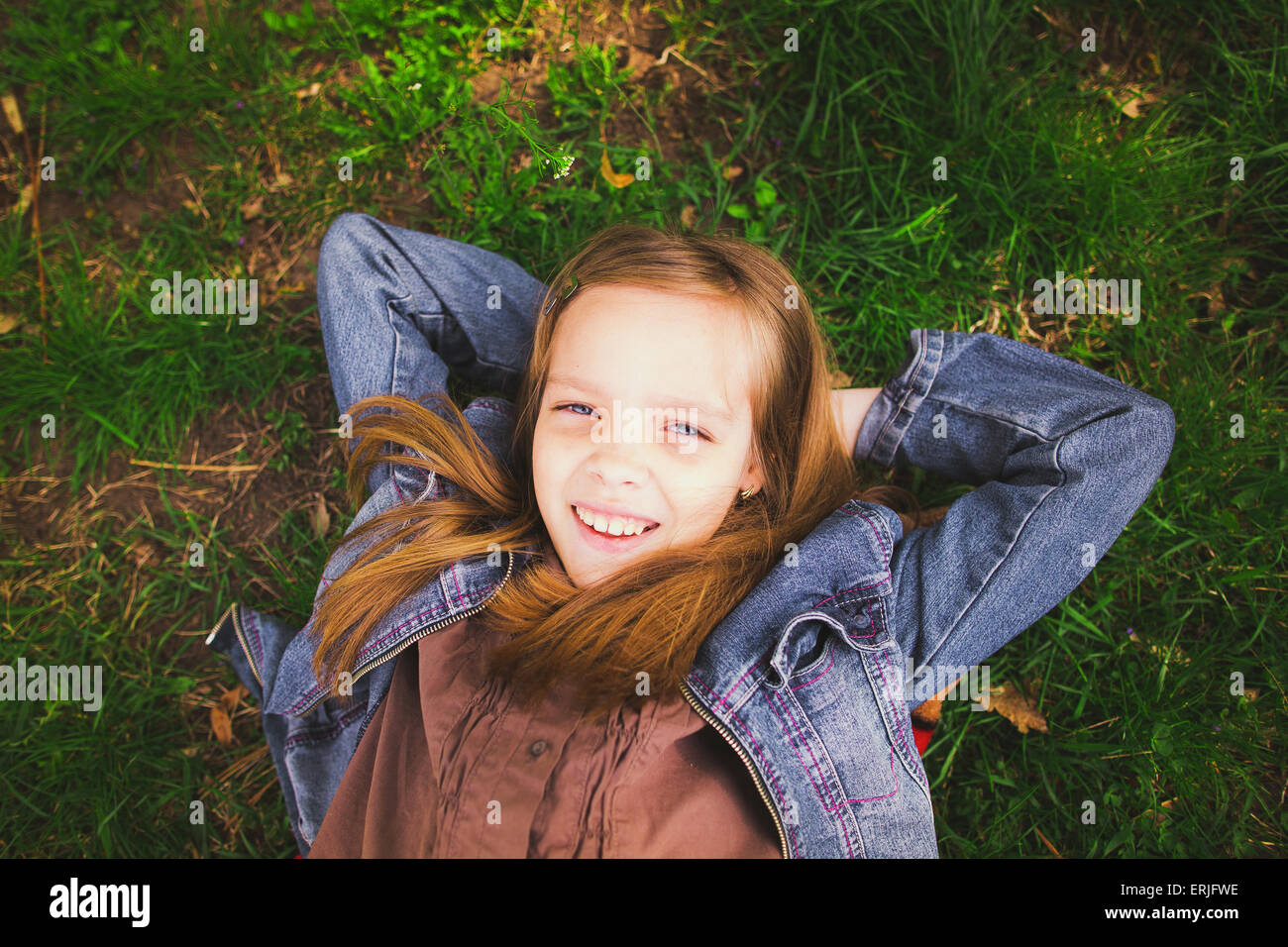 Ritratto di giovane ragazza posa sull'erba all'esterno. Bella sorridente faccia bambino. Ragazza guardando la fotocamera. Close up. Colo orizzontale Foto Stock