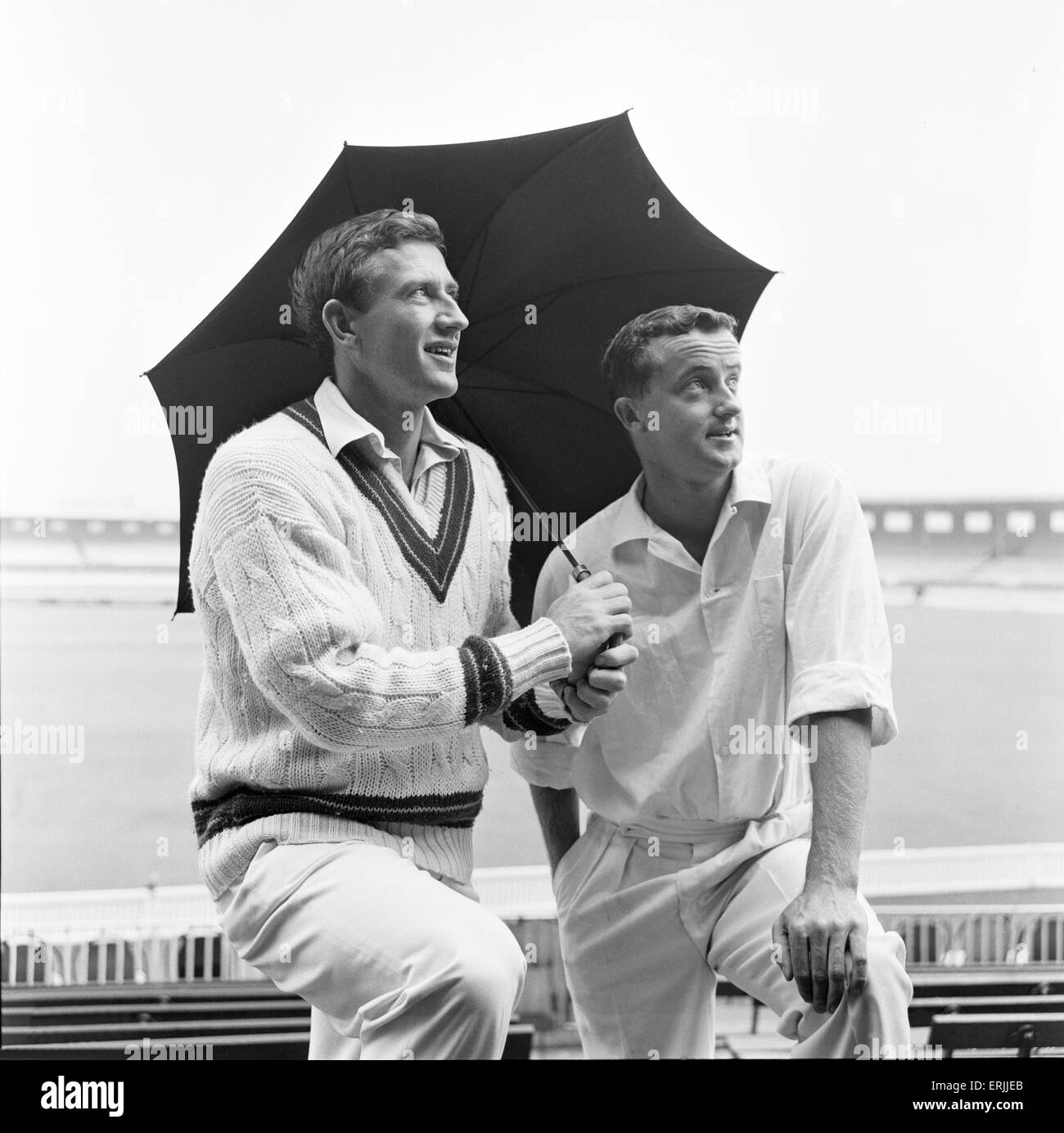 Il Cricketers australiano Graham McKenzie (sinistra) e Grahame Corling rifugio dalla pioggia sotto un ombrello a Old Trafford prima dell'Inghilterra v Australia 4 test match per le ceneri. Il 22 luglio 1964. Foto Stock