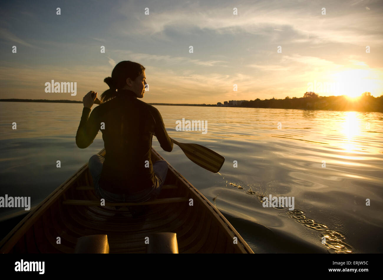 Le Maure donna si siede di fronte in legno tela canoa sul lago guardando fuori nel tramonto azienda Pala Foto Stock