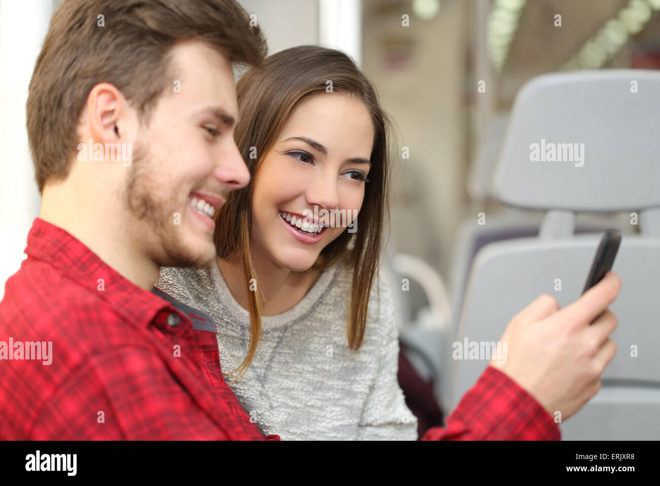 Paio di felice passeggeri condividono un telefono intelligente che viaggiano all'interno di un treno Foto Stock