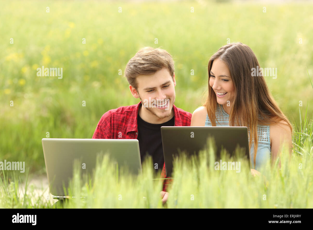 Coppia o amici a guardare le app in due notebook in un campo verde Foto Stock