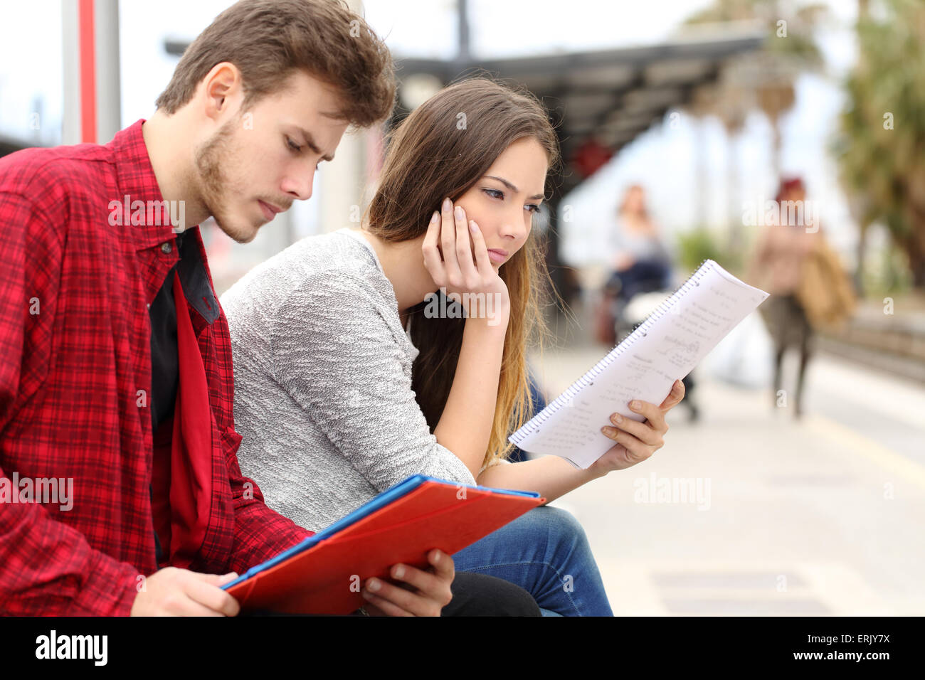 Due studenti concentrati mentre sono in attesa del trasporto in una stazione ferroviaria Foto Stock