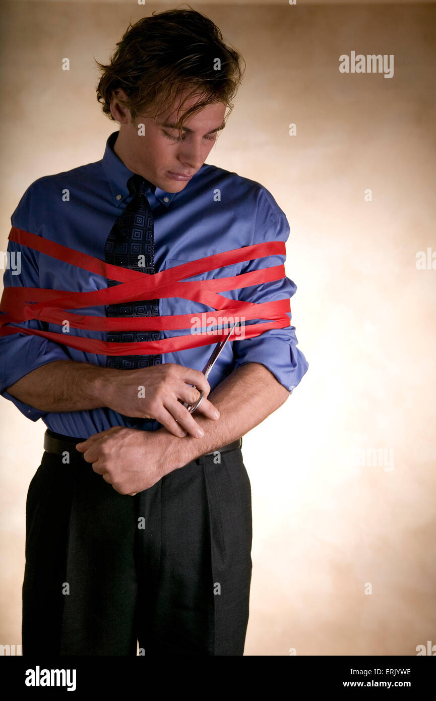 L'uomo avvolto nel nastro rosso taglia se stesso libero. Foto Stock