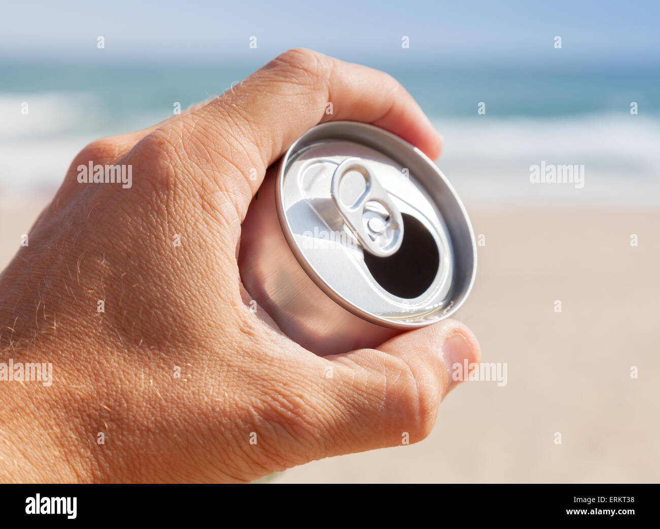 Bomboletta di alluminio di birra in mano maschio con sfocati spiaggia e mare su uno sfondo Foto Stock