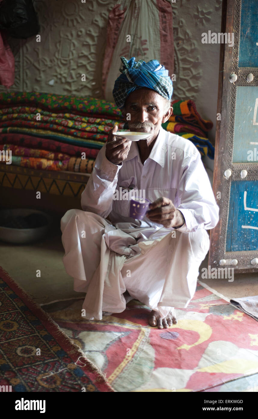 Uomo Turbanned sorseggiando un tè da piattino in casa tribali, Soyla, Kachchh, Gujarat, India Foto Stock