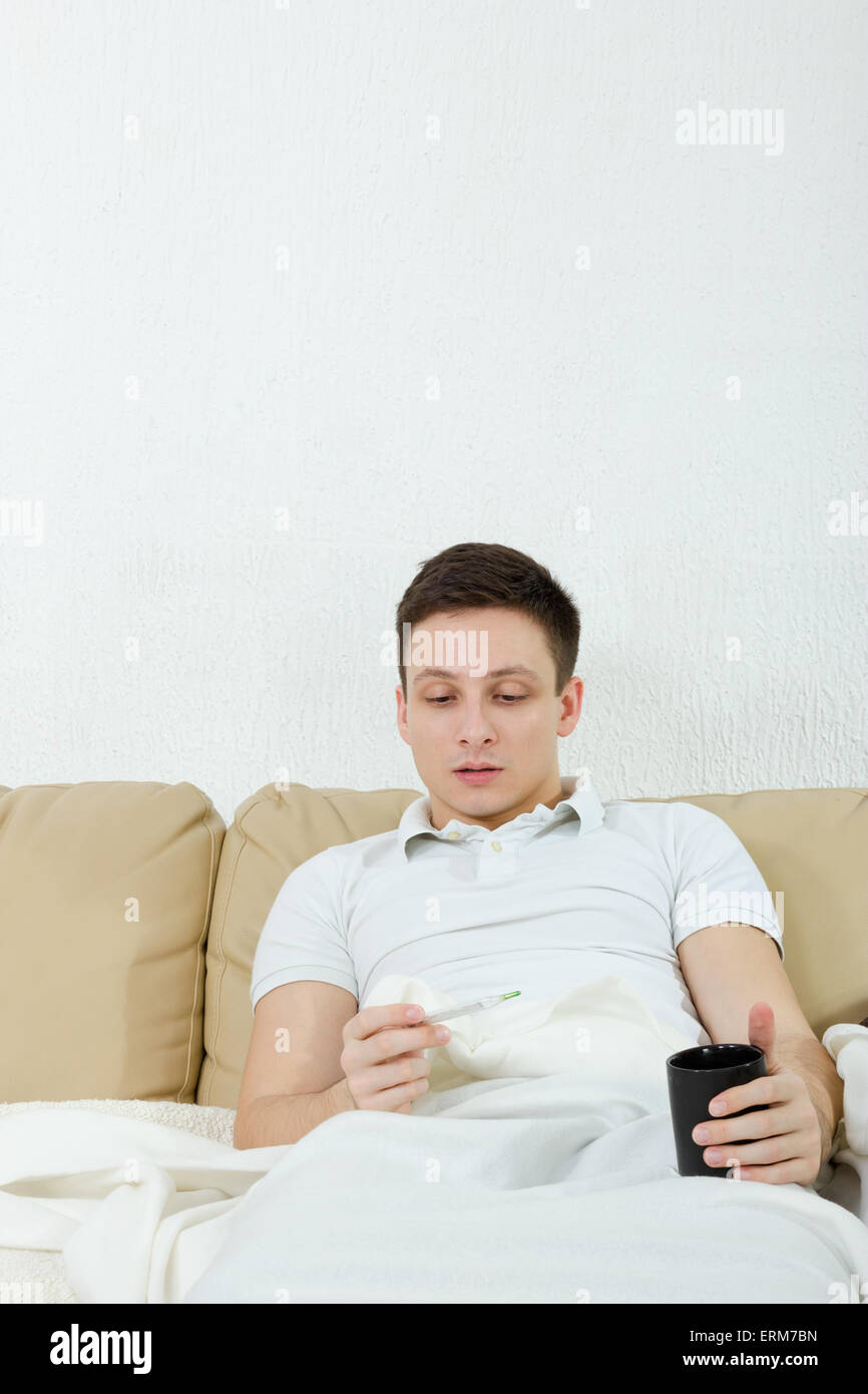 Uomo pallido malati a casa avente temperatura e influenza , giovane uomo disteso rivestito con guaina avendo la febbre e la holding e termometro Foto Stock