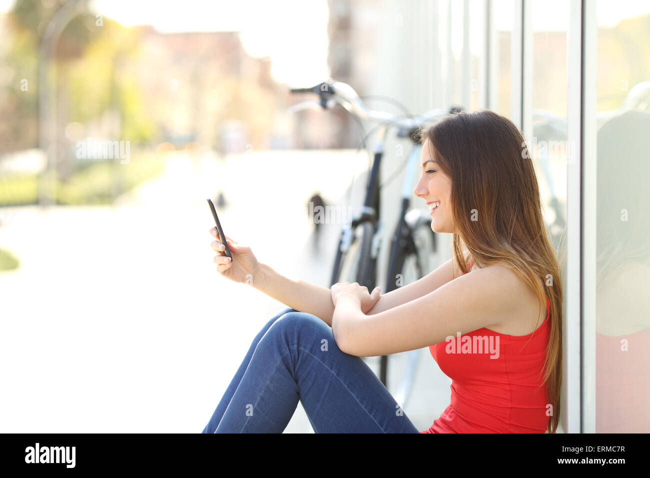 Felice ragazza seduta utilizzando un telefono cellulare in un parco accanto alla sua bicicletta Foto Stock