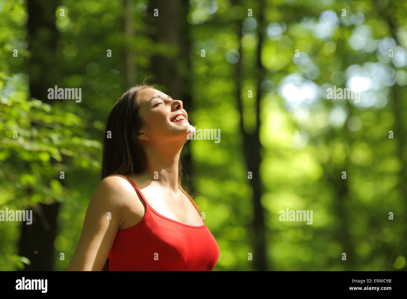 Donna respirando aria fresca in una foresta verde in estate indossa una maglietta rossa Foto Stock