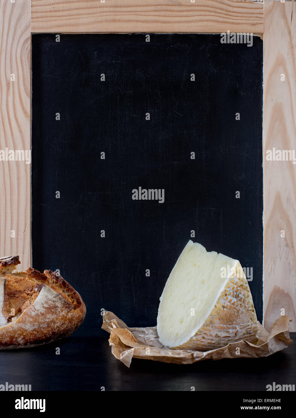 Formaggio a pasta morbida cuneo e il pezzo di pane rustico pane in parte anteriore dello sbozzato vecchia blackboard carte. Foto Stock